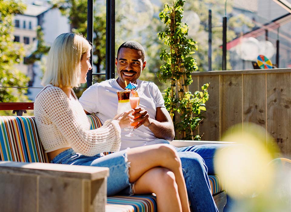 Paar sitzt auf der Papa Joe's Loung und stoss mit Cocktails in der Sonne an